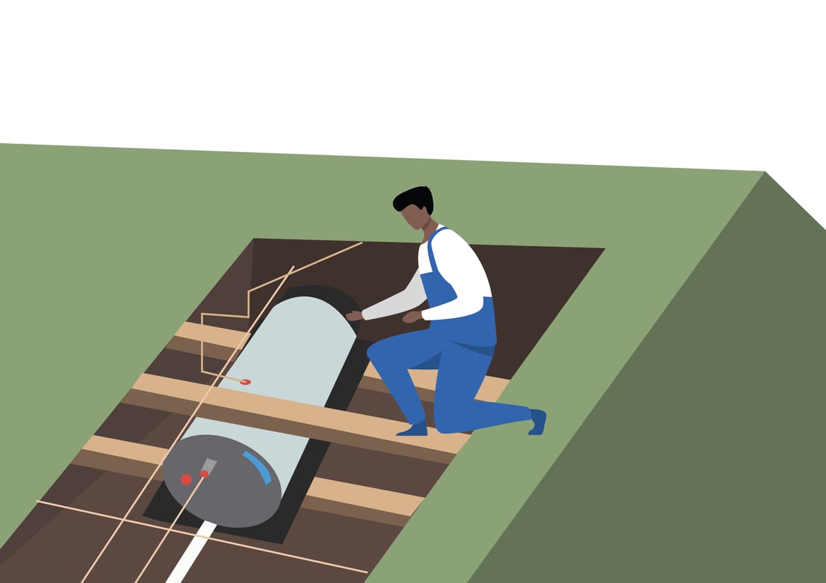 A plumber kneeling on the joists of a roof space, guiding a hot water cylinder into position on a bearer
