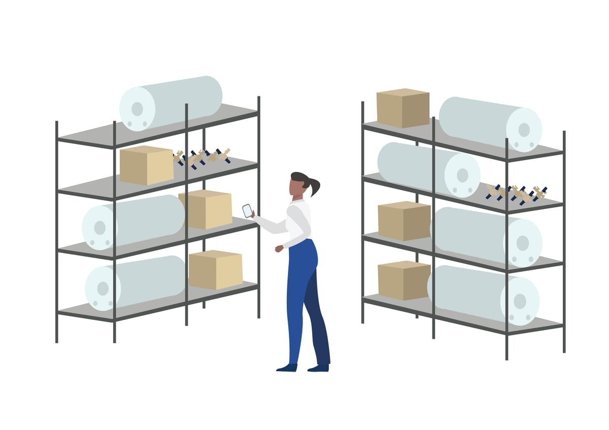 A Home Assist team member checking stock on a warehouse rack holding hot water cylinders, valve sets and compliance parts